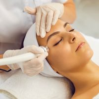 Woman receiving spa facial skin rejuvenation treatment with handheld device by esthetician