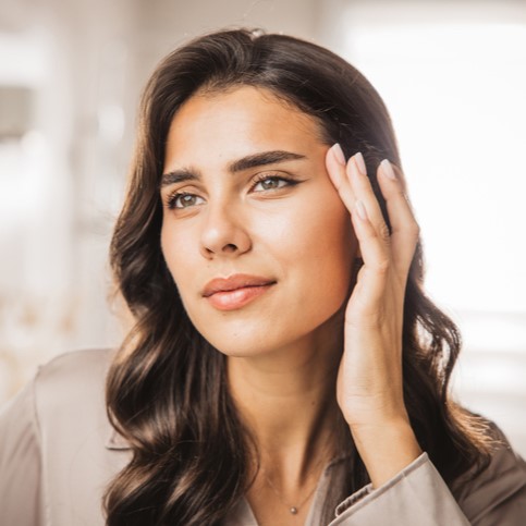 Close-up of a thoughtful woman with long dark hair touching her face in soft natural light